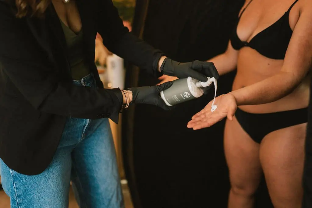 Spray tan technician in black gloves applying Sjolie Barrier Cream to client