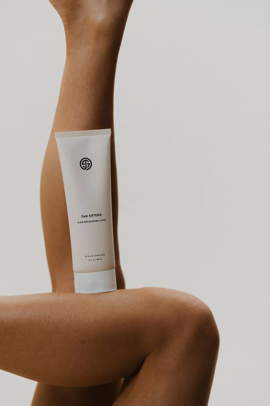 Model applying Sjolie Tan Extend Lotion to legs for daily spray tan maintenance and color extension