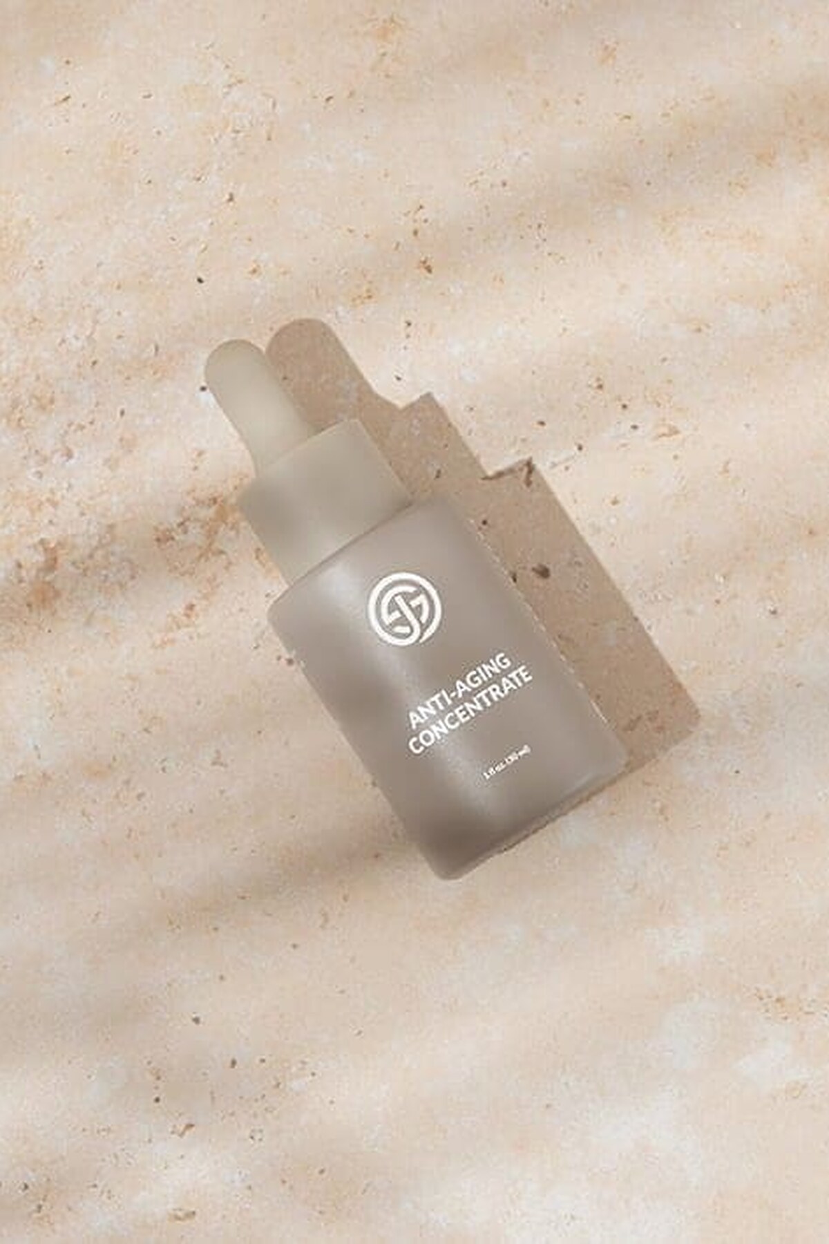 SJOLIE Anti-Aging Concentrate dropper bottle lying on sand-colored stone in soft shadow