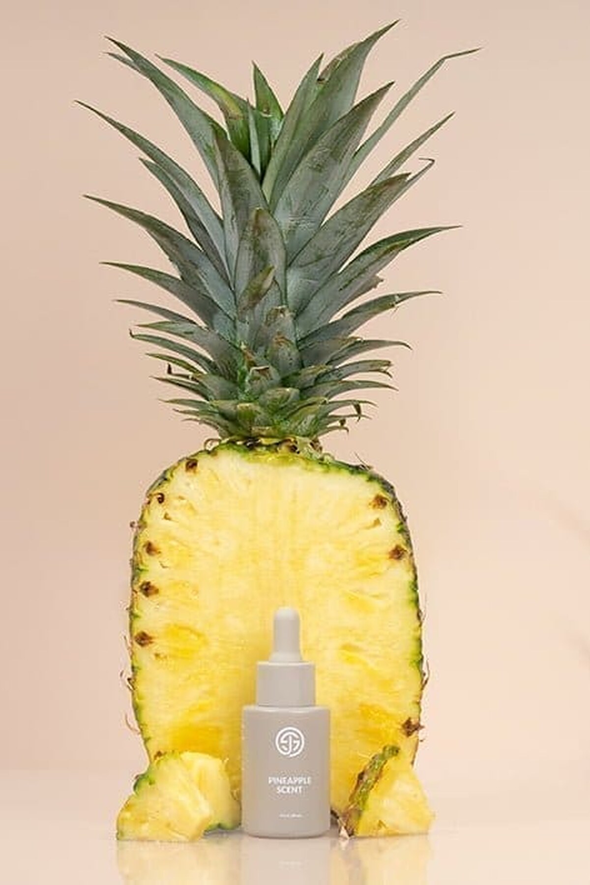 SJOLIE Pineapple Scent Drops bottle in front of a halved pineapple