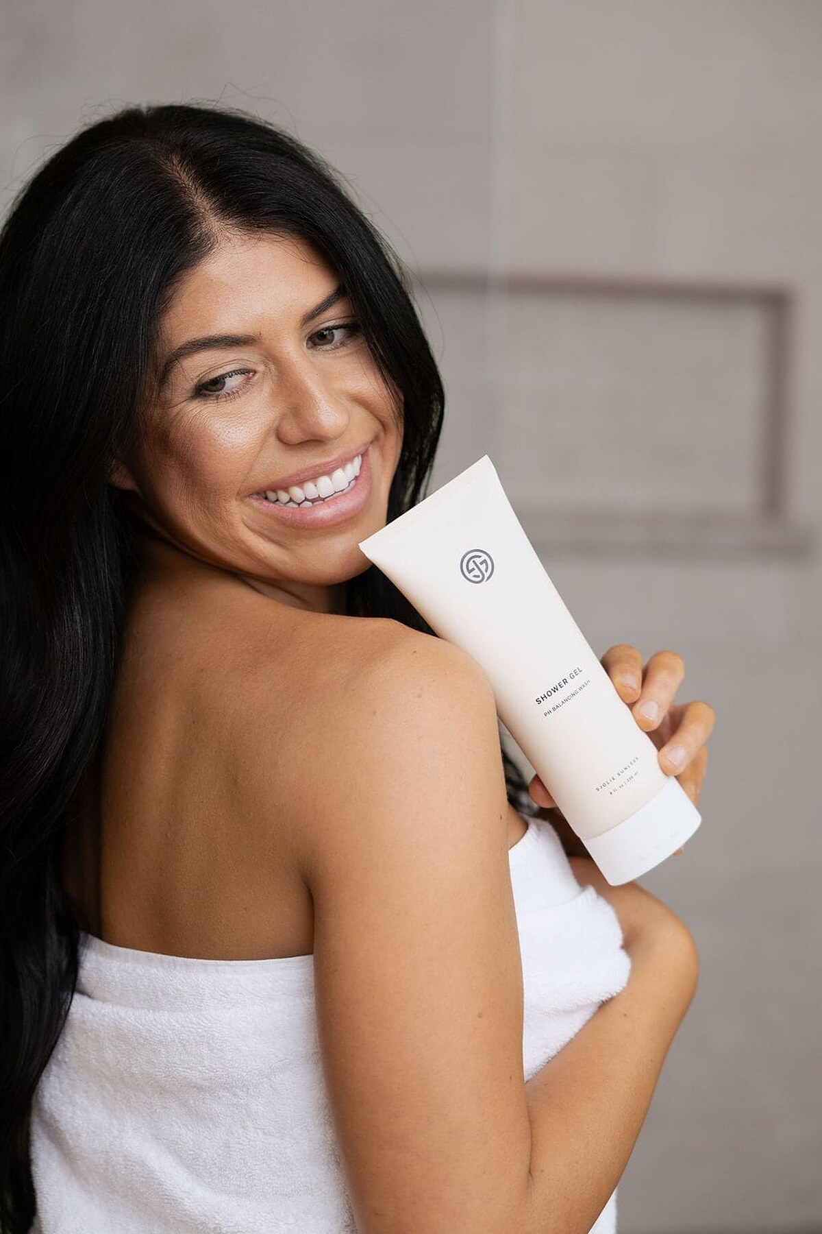 Smiling woman wrapped in a towel holding a tube of SJOLIE Shower Gel
