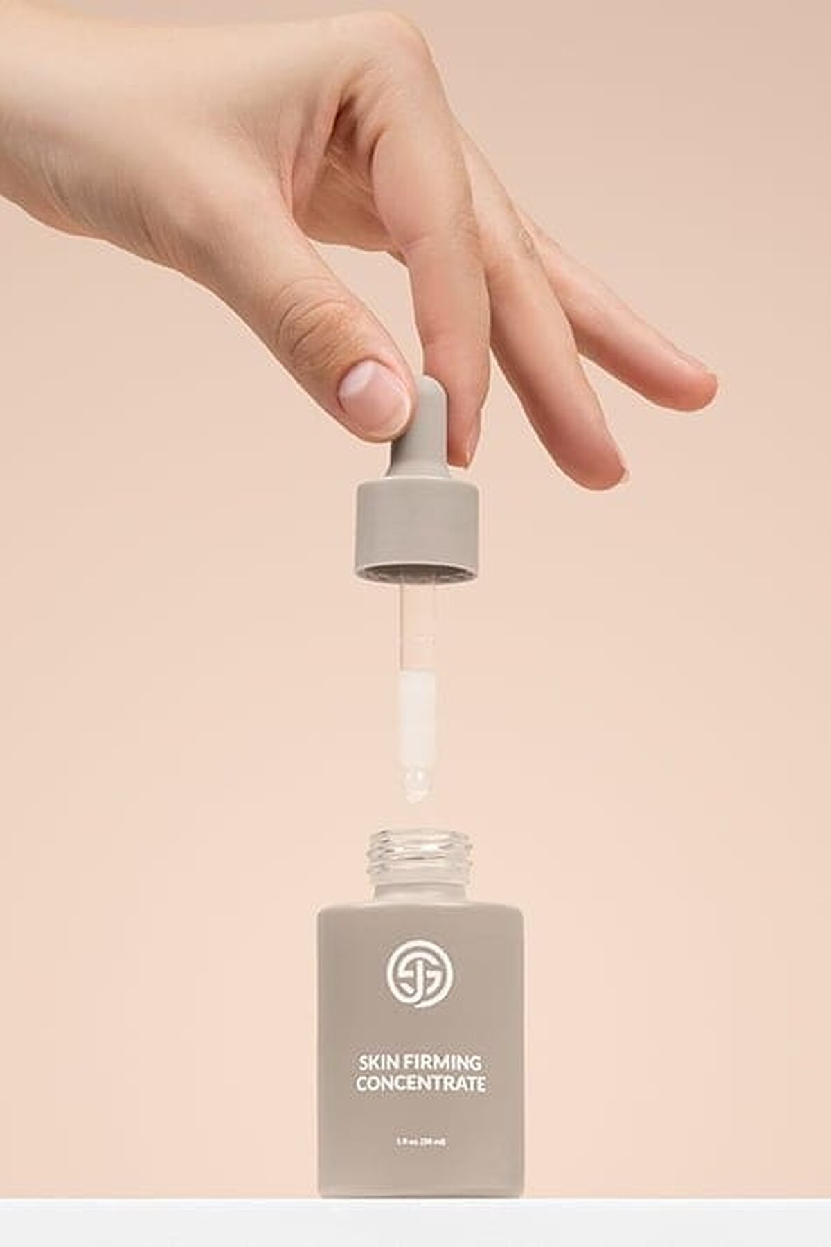 Hand lifting the dropper from a bottle of SJOLIE Skin Firming Concentrate