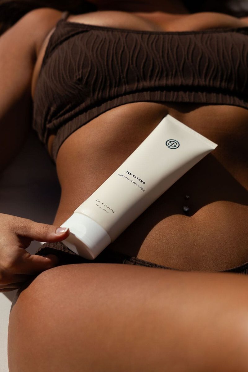 Tanned woman in a brown bikini holding a tube of SJOLIE Tan Extend Lotion against her thigh