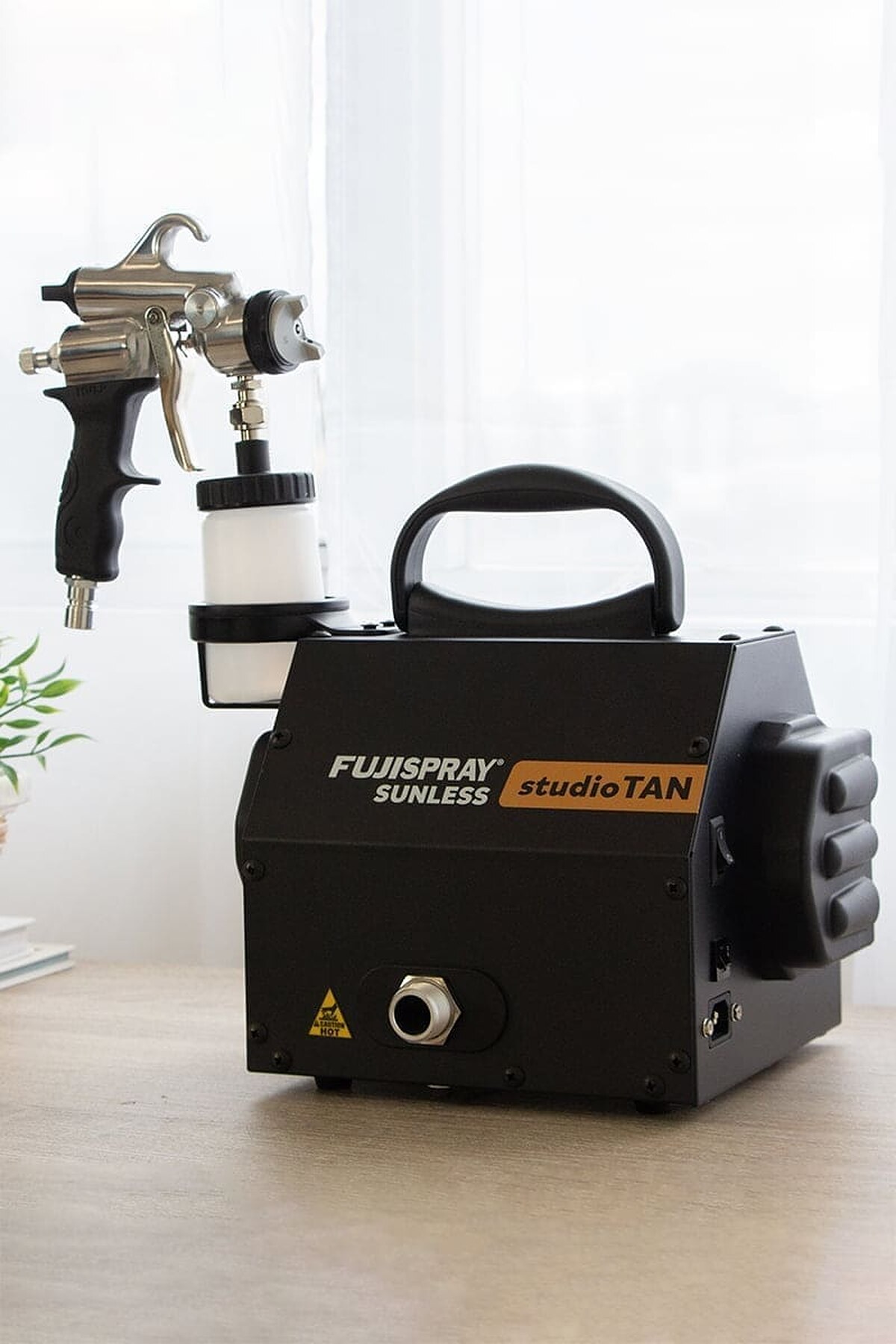 Fuji studioTAN spray tan machine on a table with its applicator resting in the cup holder