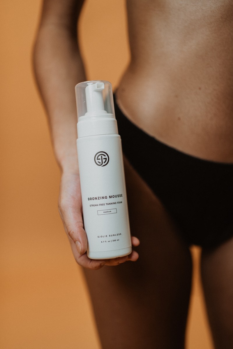 Model holding a bottle of Sjolie Bronzing Mousse streak-free self-tanning foam