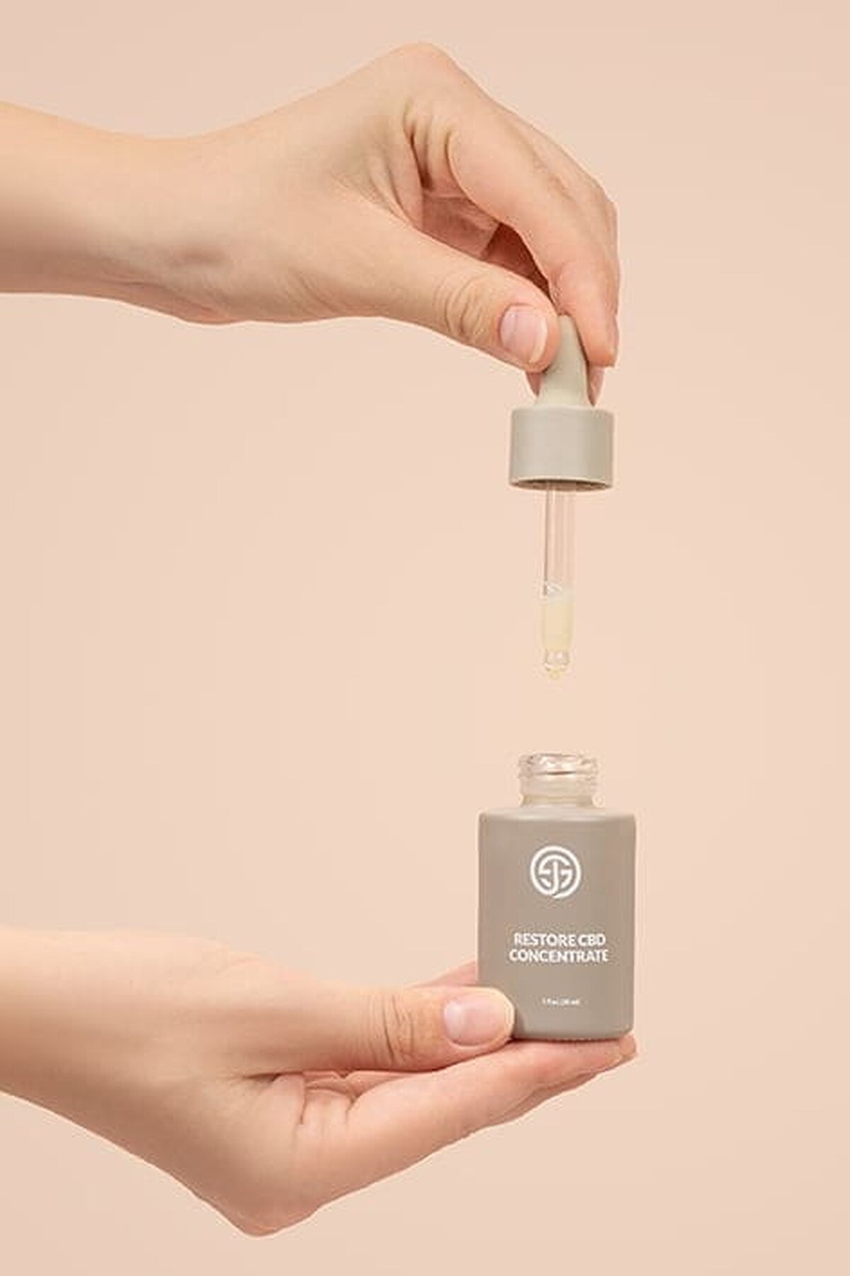 Hand lifting a dropper from SJOLIE Restore CBD Concentrate against a peach background