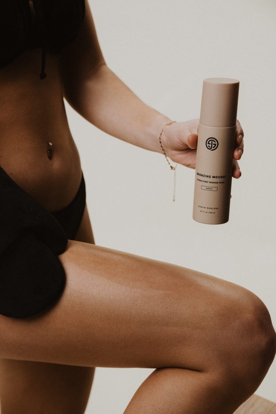 Model holding Sjolie self tan mousse bottle ready to apply