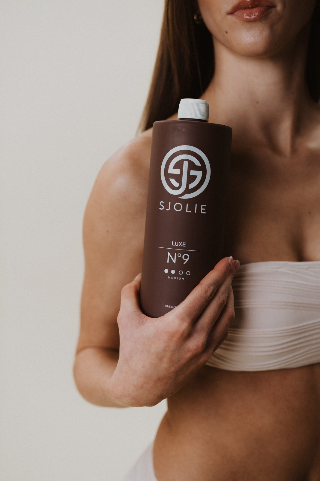 Sjolie Luxe N°9 spray tan solution bottle held by professional spray tan artist — clean-ingredient sunless tanning formula