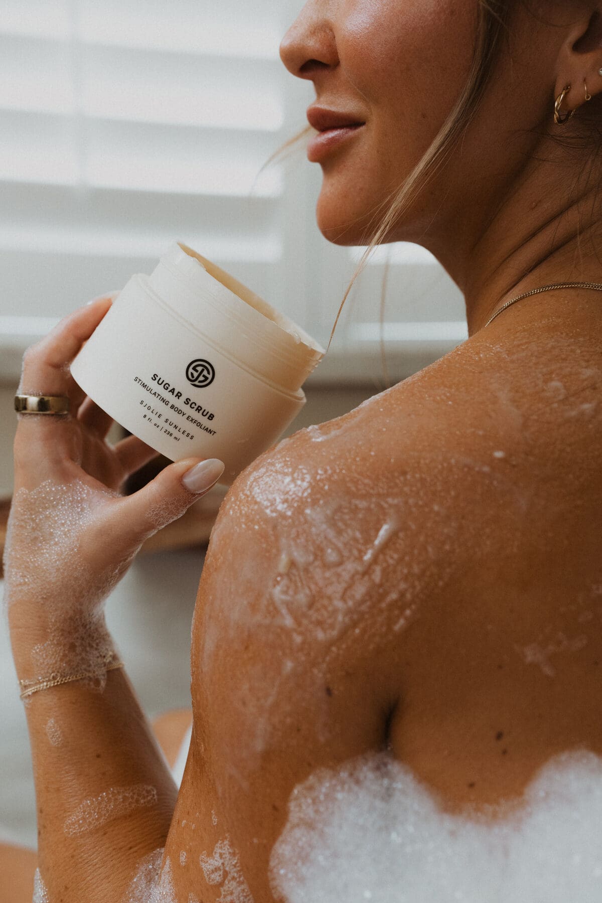 Sjolie Sugar Scrub jar held during bath ritual for smooth skin