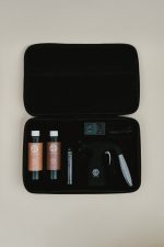 Open Sjolie wireless spray tan kit case showing the cordless gun, battery, charging cable, extra cup and Original N°9 and Luxe N°12 solution samples