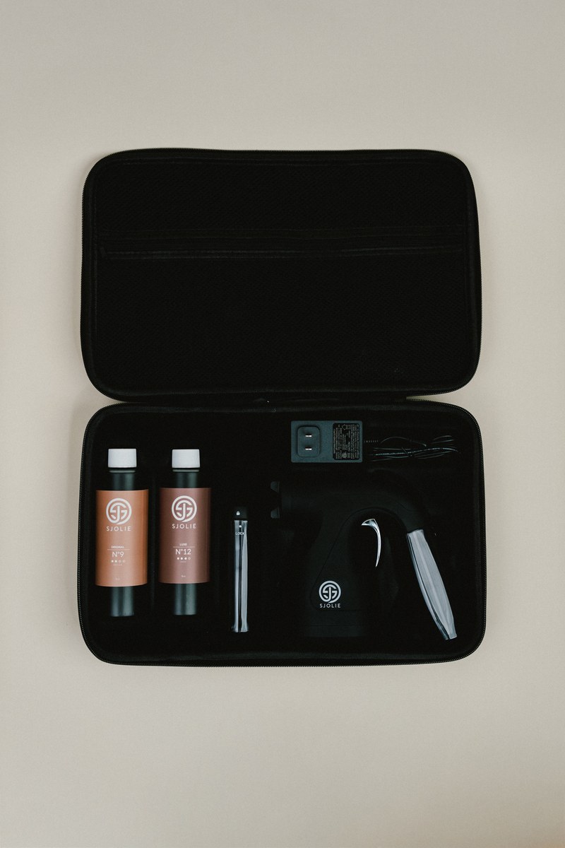 Open Sjolie wireless spray tan kit case showing the cordless gun, battery, charging cable, extra cup and Original N°9 and Luxe N°12 solution samples