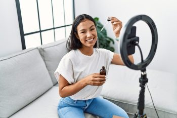 Smiling beauty content creator recording a skincare tutorial video with a ring light and smartphone