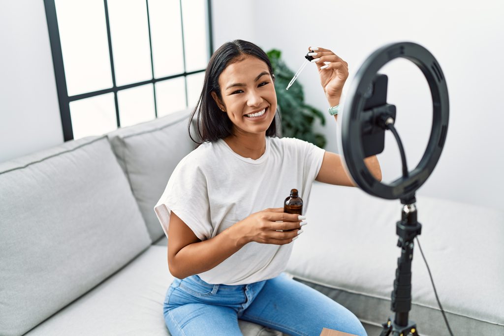 Smiling beauty content creator recording a skincare tutorial video with a ring light and smartphone