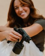 Spray tan artist holding the Sjolie X1 Pro professional spray tan machine in matte black