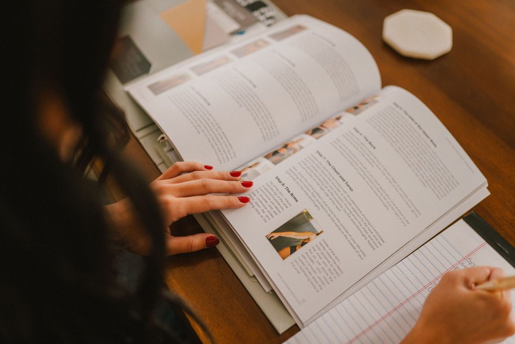 Student studying Sjolie spray tan training handbook with airbrush tanning technique instructions